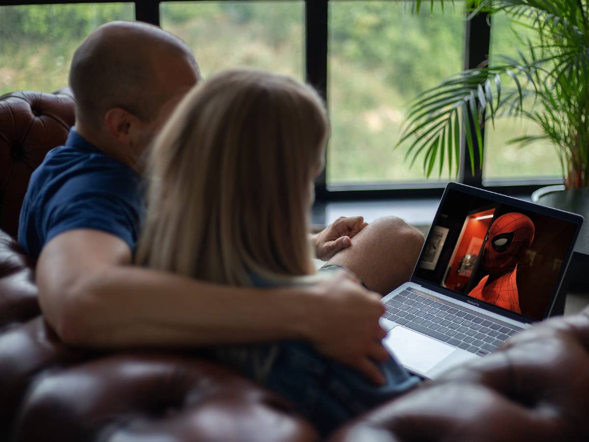Eine Frau und ein Mann schauen auf einem Laptop von einer Couch aus einen Film.