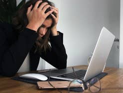 Frau sitzt verzweifelt vor einem MacBook und rauft sich die Haare.