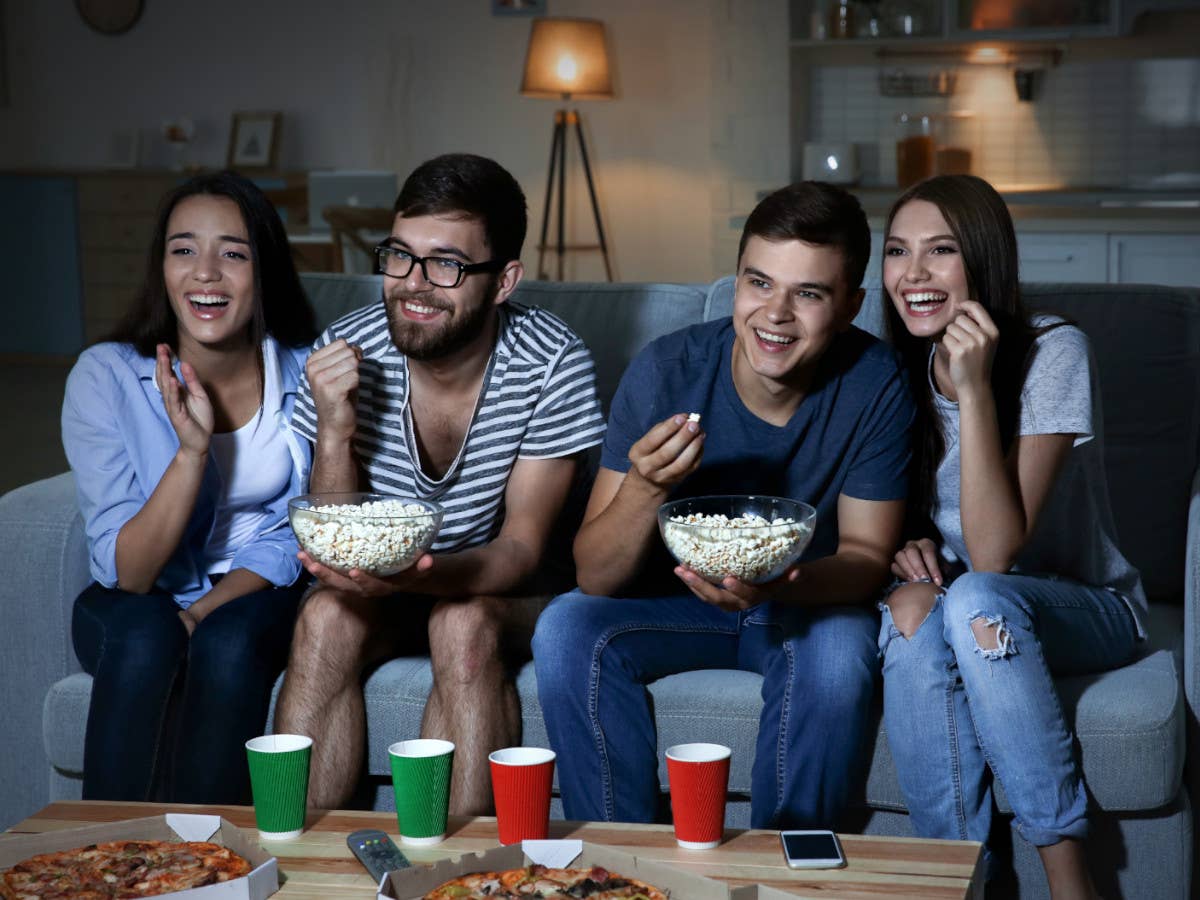 Vier Freunde sitzen auf einer Couch, essen Popcorn und streamen einen DC-Film.