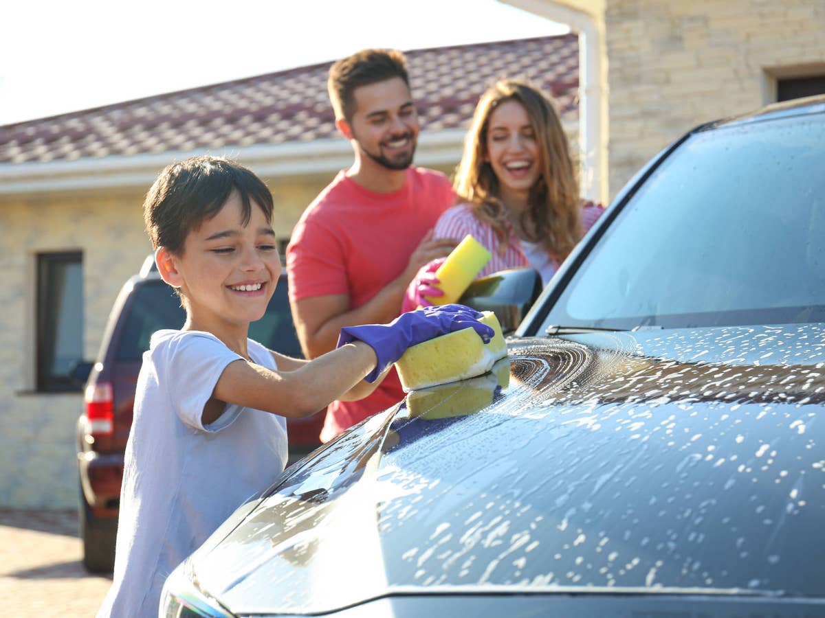 Familie wäscht gemeinsam ein Auto und hat viel Spaß dabei.