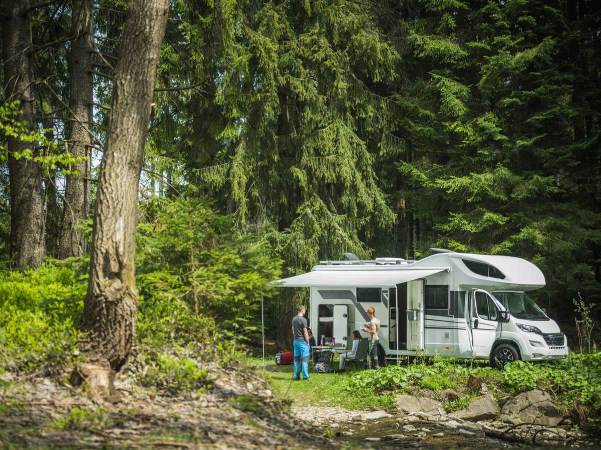 Für Wohnmobile, Camper-Vans, Boote oder Tiny Houses: Diese Energielösungen sind perfekt für ein Leben Ein Wohnmobil steht in einem sonnigen Wald. Davor stehen und sitzen ein paar Menschen.
