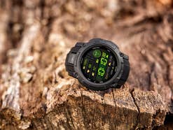 Garmin Instinct 3 Tactical Edition Uhr auf einer Holzoberfläche, die Uhrzeit, Herzfrequenz und Batteriestand anzeigt.