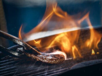 Fleisch wird auf einem Grill unter offener Flamme gewendet