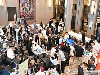 Vogelperspektive auf einen Hotelsaal mit mehreren Reihen von Ausstellungstischen, an denen Besucher und Standpersonal der Global Connect Show Technikprodukte zeigen und testen, im Hintergrund ein Werbebanner von Vevor.