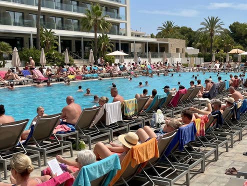 Ein Hotelpool mit meheren Liegen, die alle von Gästen besetzt sind. Im Pool schwimmen weitere Personen.