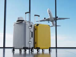 Zwei Koffer am Flughafen mit einem startenden Flugzeug im Hintergrund