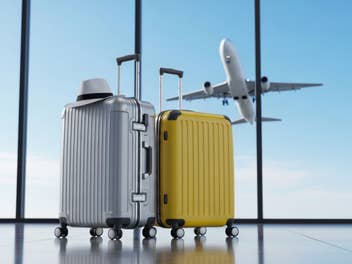 Zwei Koffer am Flughafen mit einem startenden Flugzeug im Hintergrund