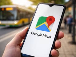 Google Maps Logo auf einem Smartphone, im Hintergrund ein Bus