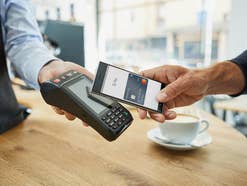 Ein Handy mit Google-Pay-App wird im Café an ein Kartenterminal gehalten