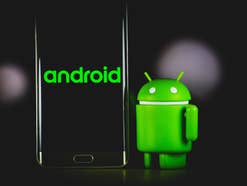 Android-Figur steht vor einem Android-Smartphone vor schwarzem HIntergrund.