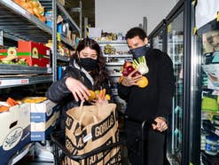 Zwei Mitarbeiter sammeln Lebensmittel ein und verpacken sie in eine Tüte