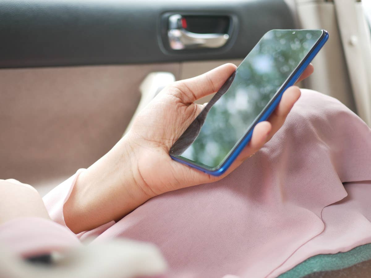 Eine Person sitzt in einem Auto und hält ein Handy in der Hand.