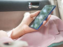 Eine Person sitzt in einem Auto und hält ein Handy in der Hand.