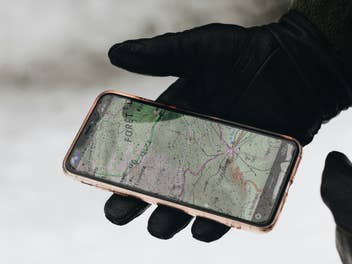 Ein dreckigs Smartphone in einer behandschuhten Hand.