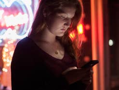 Eine Frau steht im Neonlicht mit ihrem Handy in der Hand.
