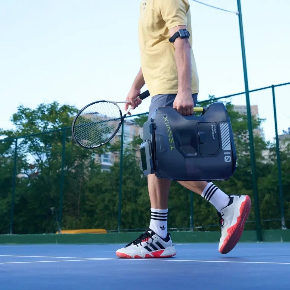 Ein Mann trägt die Tenniix Pro Ballmaschine über einen Platz