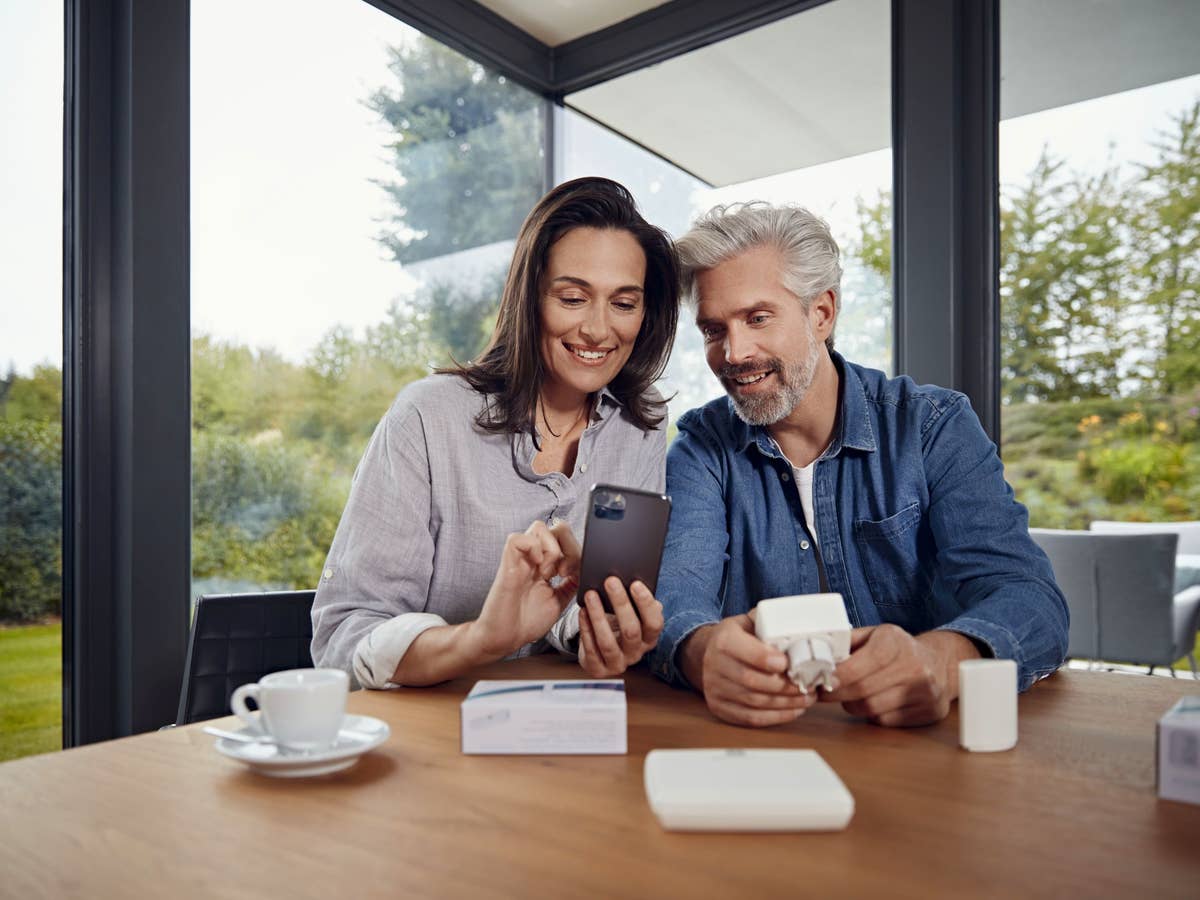 Ein Paar sitzt mit Smart-Home-Komponenten und einem Smartphone an einem Tisch