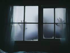 Die Silhouette einer Person zeichnet sich an einem Fenster ab, wie in einem Horrorfilm.