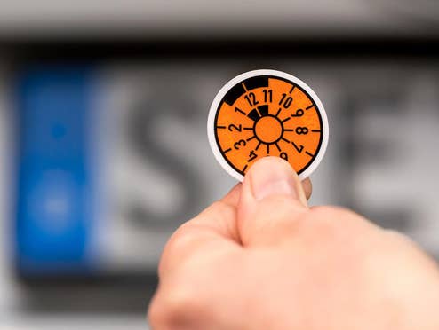 Neue Regel: Dein nächstes Auto bekommt 2 starke Upgrades Hauptuntersuchung-Plakette vor einem Nummernschild