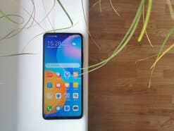 Das Huawei P smart 2021 mit aktivem Display auf einer weißen Fensterbank mit Holz und Pflanzen im Hintergrund
