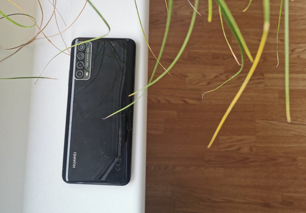 Die schwarze Rückseite des Huawei P smart 2021 auf einer weißen Fensterbank mit Holz und Pflanzen im Hintergrund.