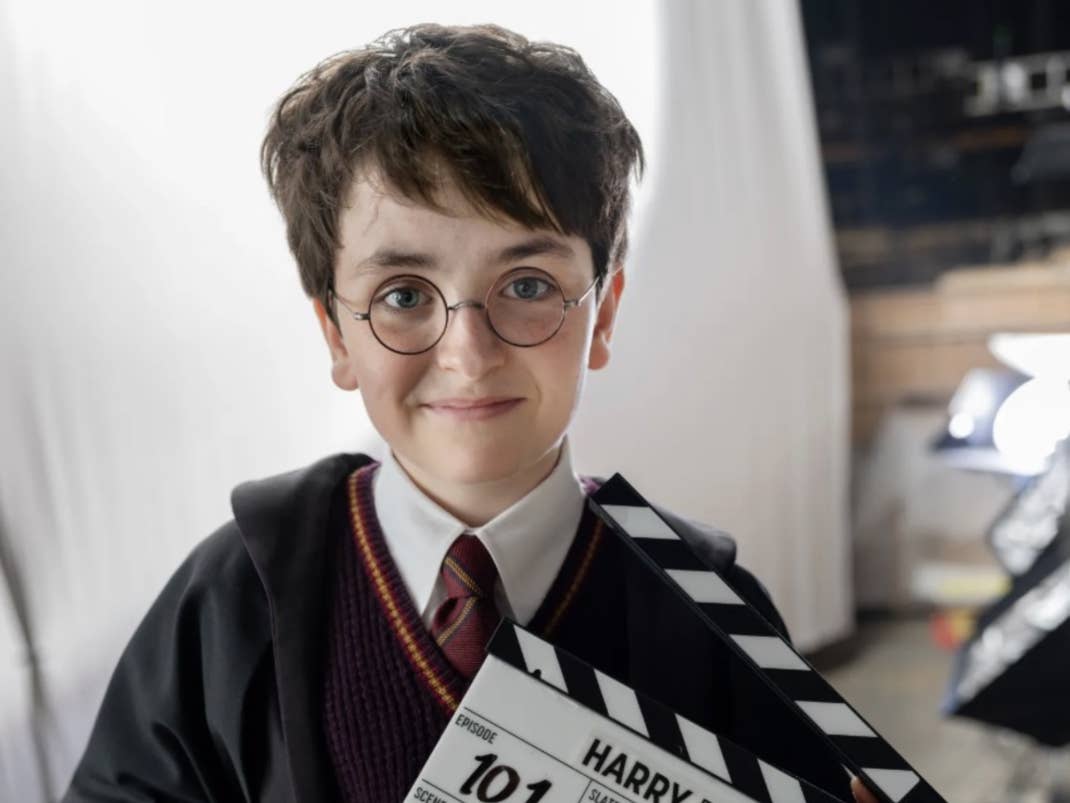 Ein junger Junge mit Brille, der einen Hogwarts-Mantel trägt und ein Klappbrett mit der Aufschrift 'HARRY POTTER' hält.