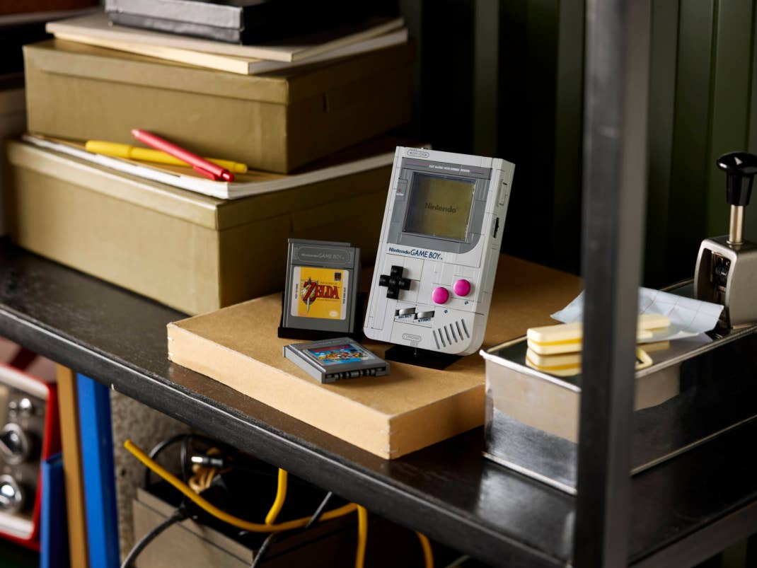Ein vintage Game Boy mit Spielkassetten auf einem überfüllten Regal zwischen Kisten und Schreibwaren.
