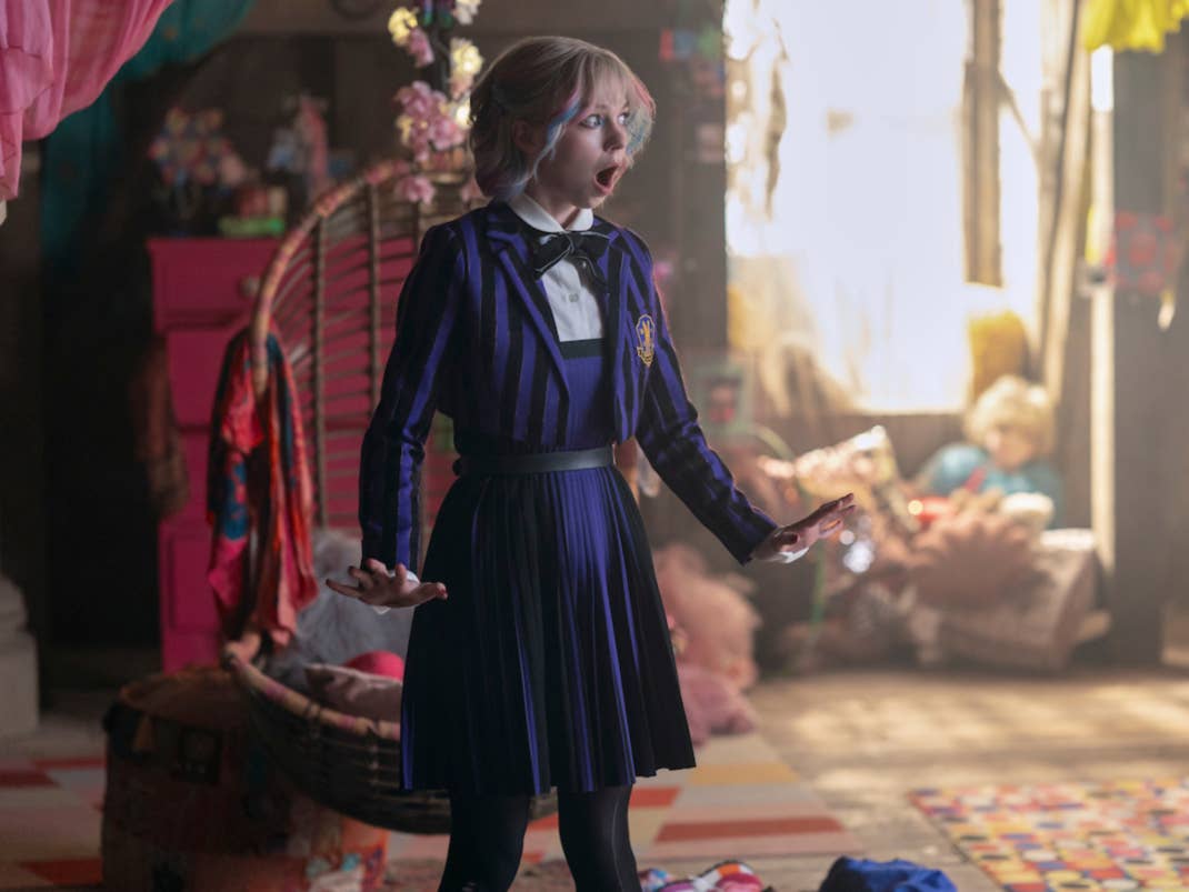 Ein überraschter Mädchen in einem gestreiften Outfit steht in einem bunten Zimmer voller Spielzeug und Dekorationen.