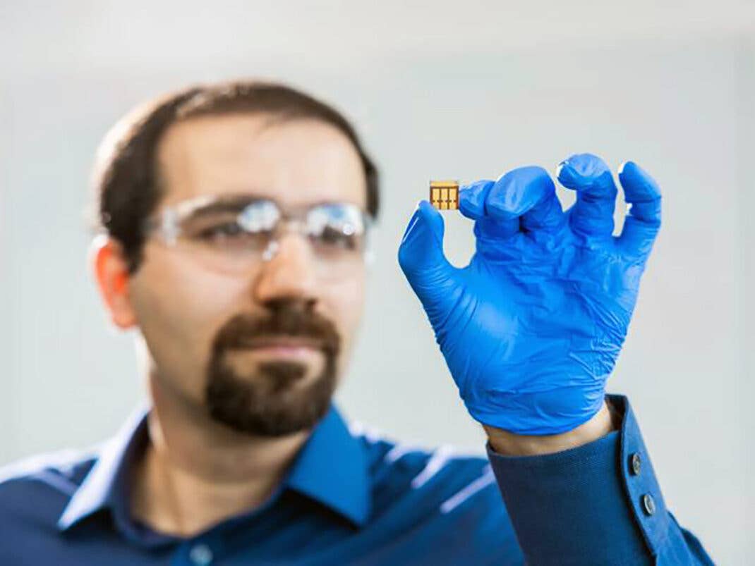 Ein Forscher in blauem Hemd und Handschuhen hält eine kleine Solarzelle, die für Innenlichtoptimierung entwickelt wurde.