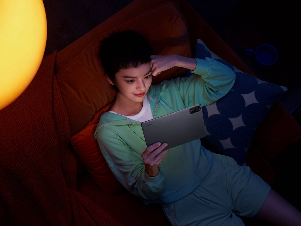 Eine Person, die sich auf einem Sofa entspannt und ein Xiaomi Redmi Pad 2 Tablet in einem schwach beleuchteten Raum verwendet.