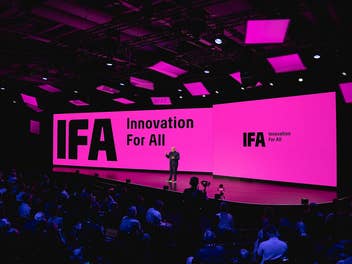 Ein Redner steht auf einer großen Bühne vor zwei pinkfarbenen Leinwänden mit der Aufschrift „IFA Innovation For All