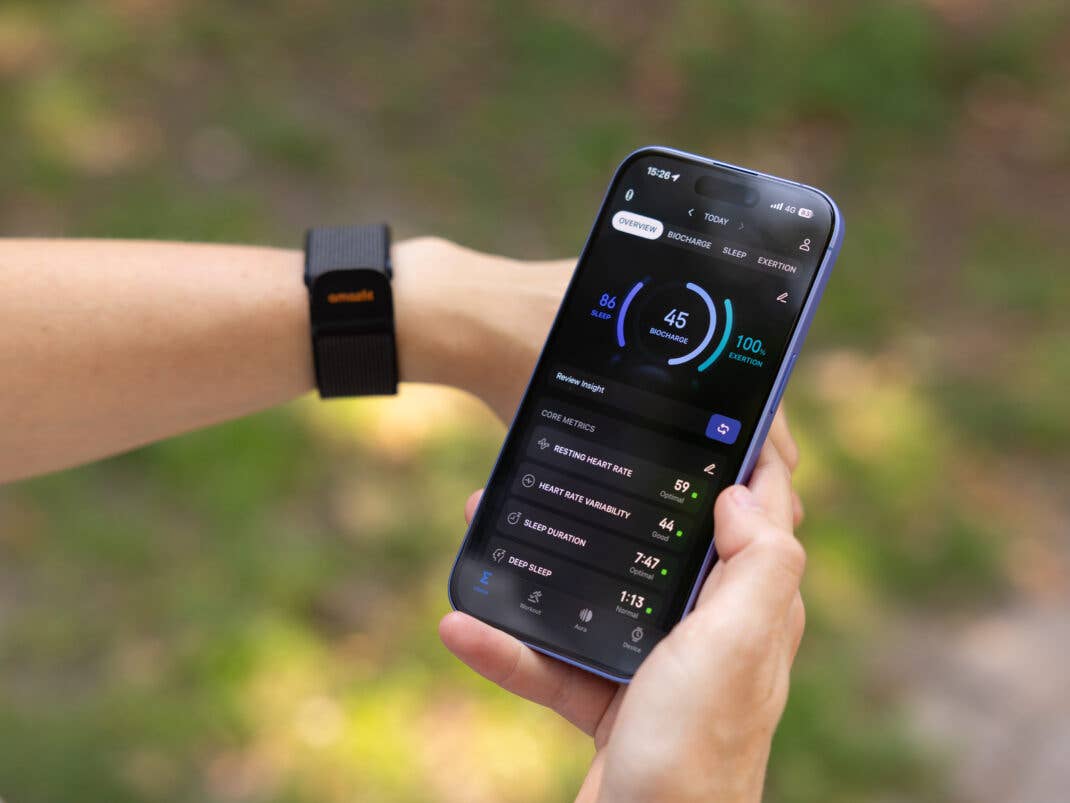 Eine Person überprüft Gesundheitsmetriken auf einem Smartphone und trägt ein Amazfit Helio-Armband am Handgelenk.