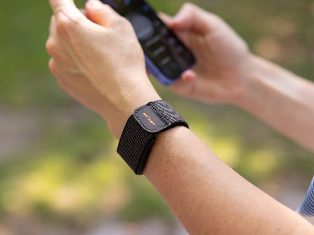 Eine Nahaufnahme eines Handgelenks mit einem Amazfit Helio-Armband, das ein Smartphone hält.