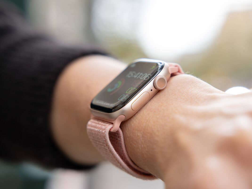 Nahaufnahme einer Apple Watch an einem Handgelenk mit einem pinken Armband, die Uhrzeit und Fitnessmetriken anzeigend.