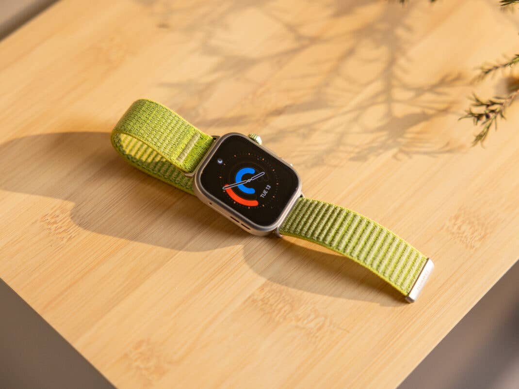 Eine Huawei Watch Fit 4 Pro mit grünem Armband auf einer Holzoberfläche, die ein buntes Zifferblatt zeigt.