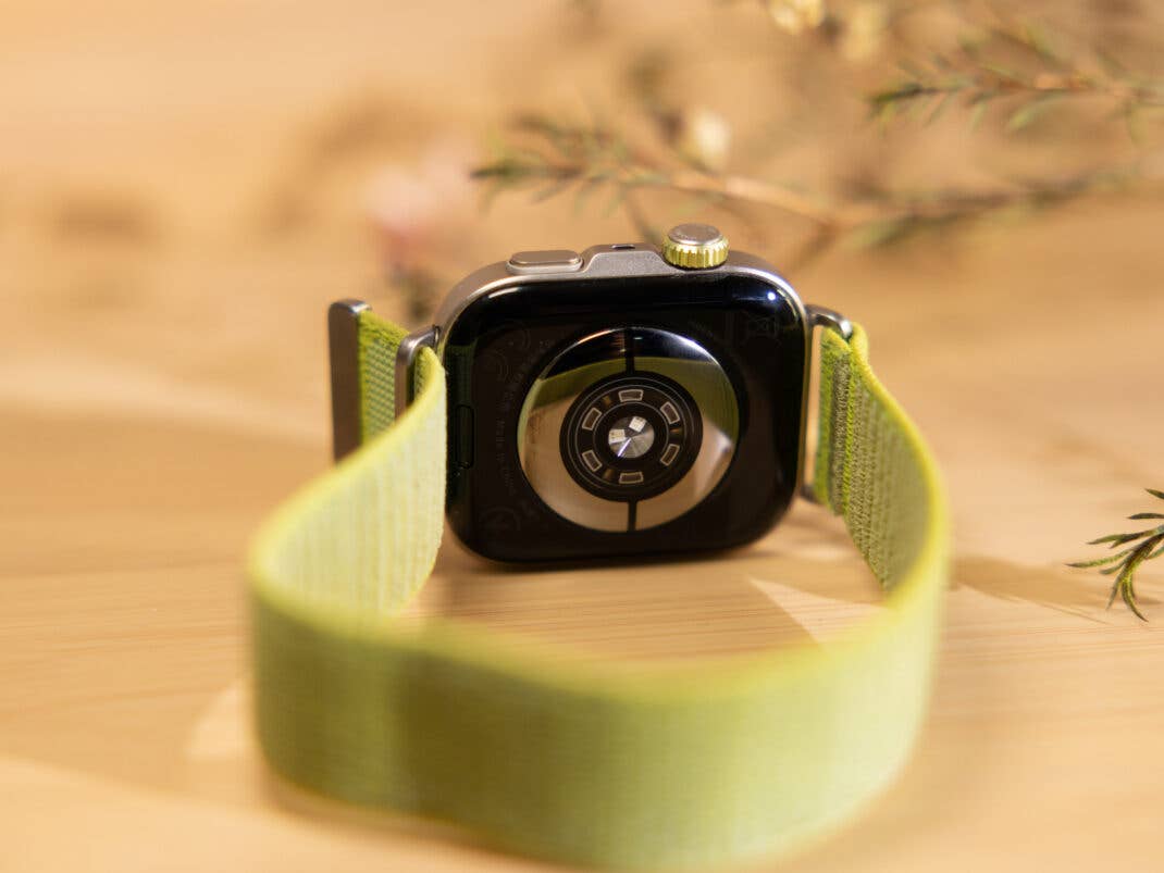 Rückansicht einer Huawei Watch Fit 4 Pro mit grünem Armband auf einer Holzoberfläche.