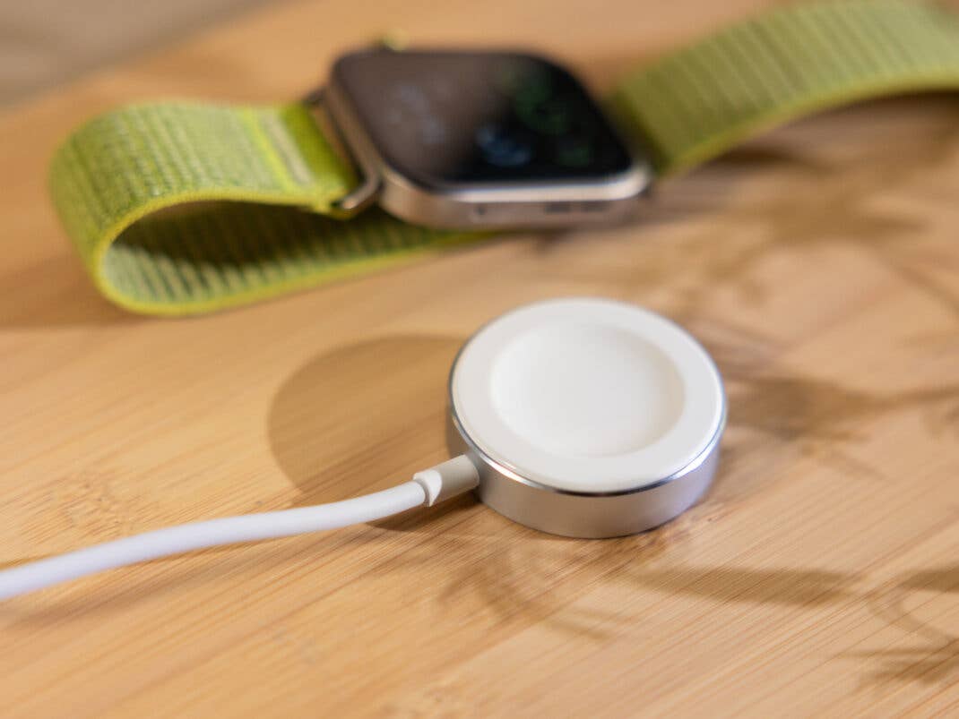 Eine Huawei Watch Fit 4 Pro mit grünem Armband neben ihrer runden Ladestation auf einer Holzoberfläche.