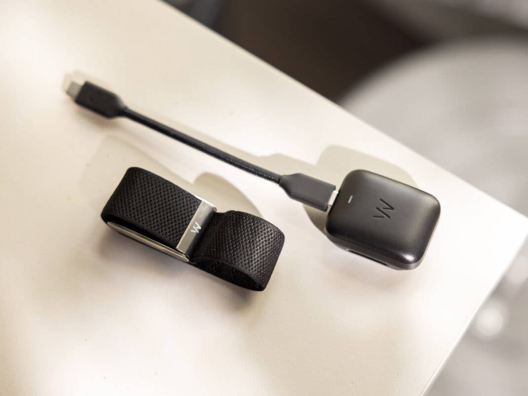 Ein schwarzes tragbares Gerät mit einem Armband und einem Ladekabel auf einer weißen Fläche.