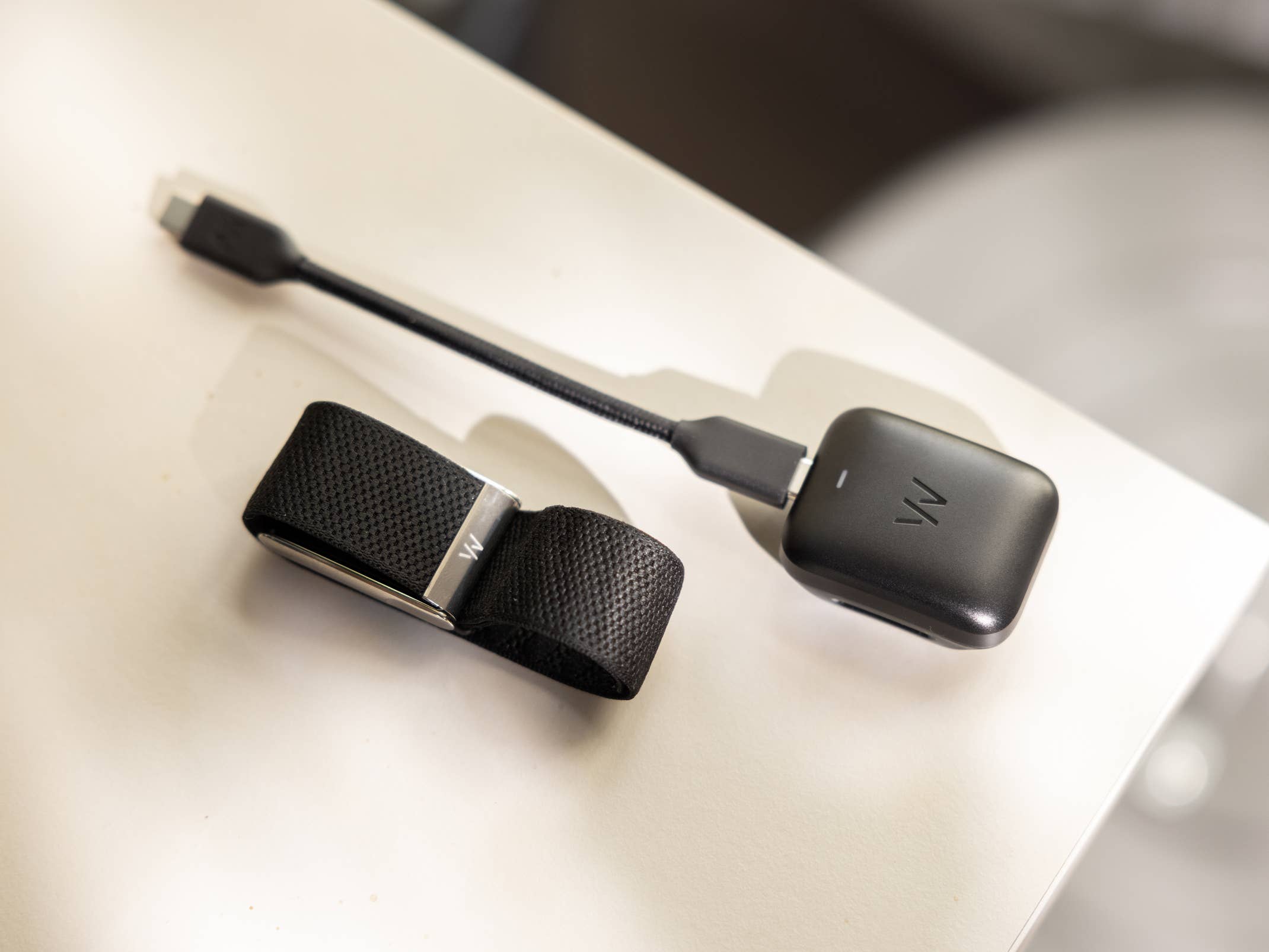 Ein schwarzes tragbares Gerät mit einem Armband und einem Ladekabel auf einer weißen Fläche.