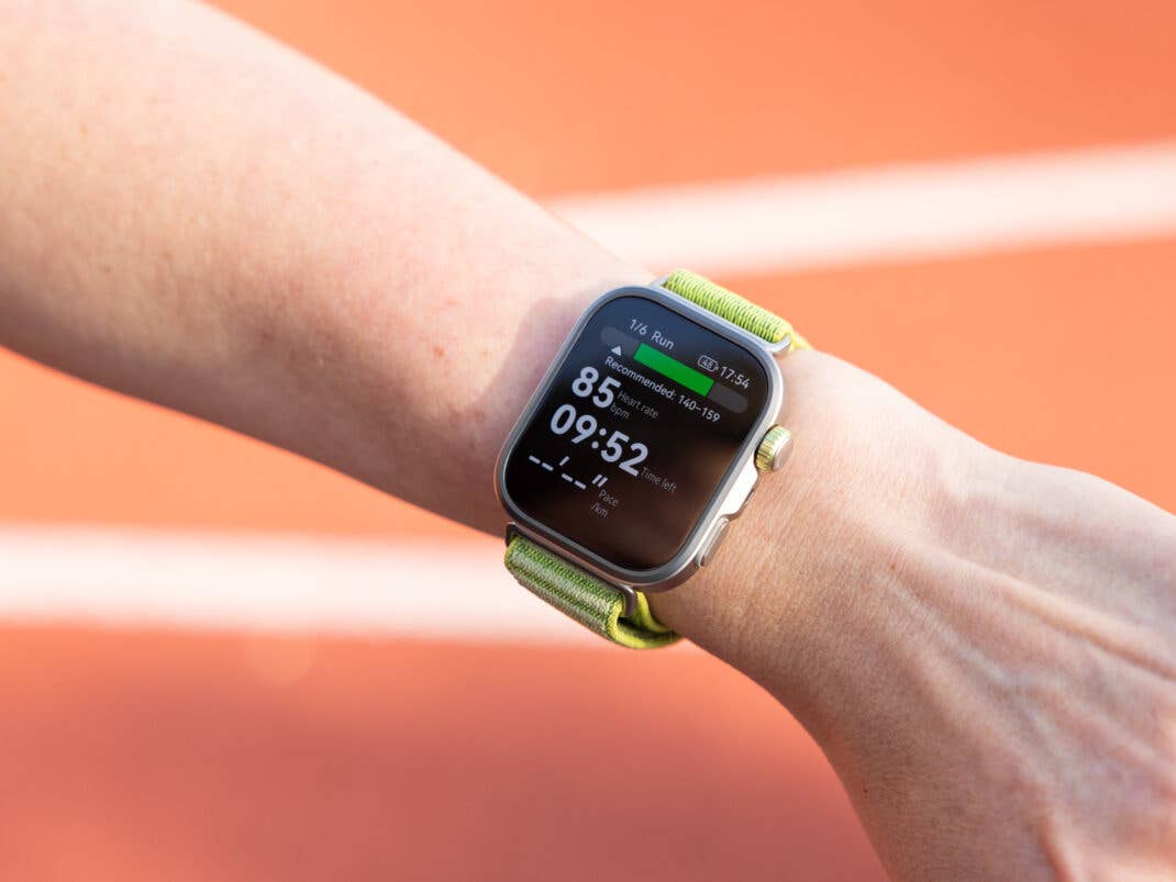 Eine Nahaufnahme einer Huawei Watch Fit 4 Pro am Handgelenk, die Herzfrequenz und Timer vor einem Laufbahn-Hintergrund anzeigt.