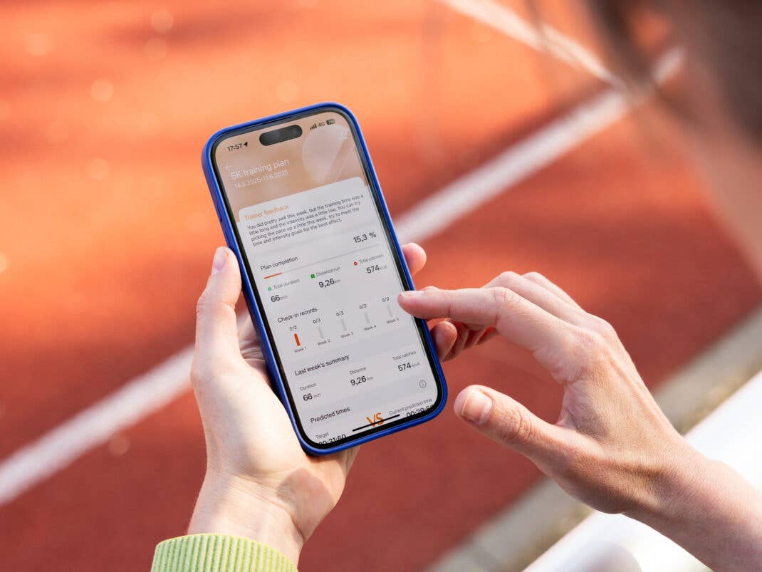 Eine Person hält ein Smartphone, das einen 5K-Trainingsplan mit Leistungskennzahlen auf einer Laufbahn anzeigt.