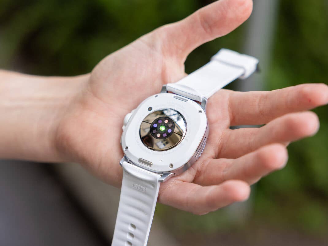 Eine Person hält eine Samsung Galaxy Watch 8 Classic, die ihre Rückseite mit Sensoren und einem weißen Armband zeigt.