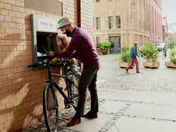 Ein Mann und ein Kind stehen mit einem Fahrrad vor einem ING DiBa Bankautomat.