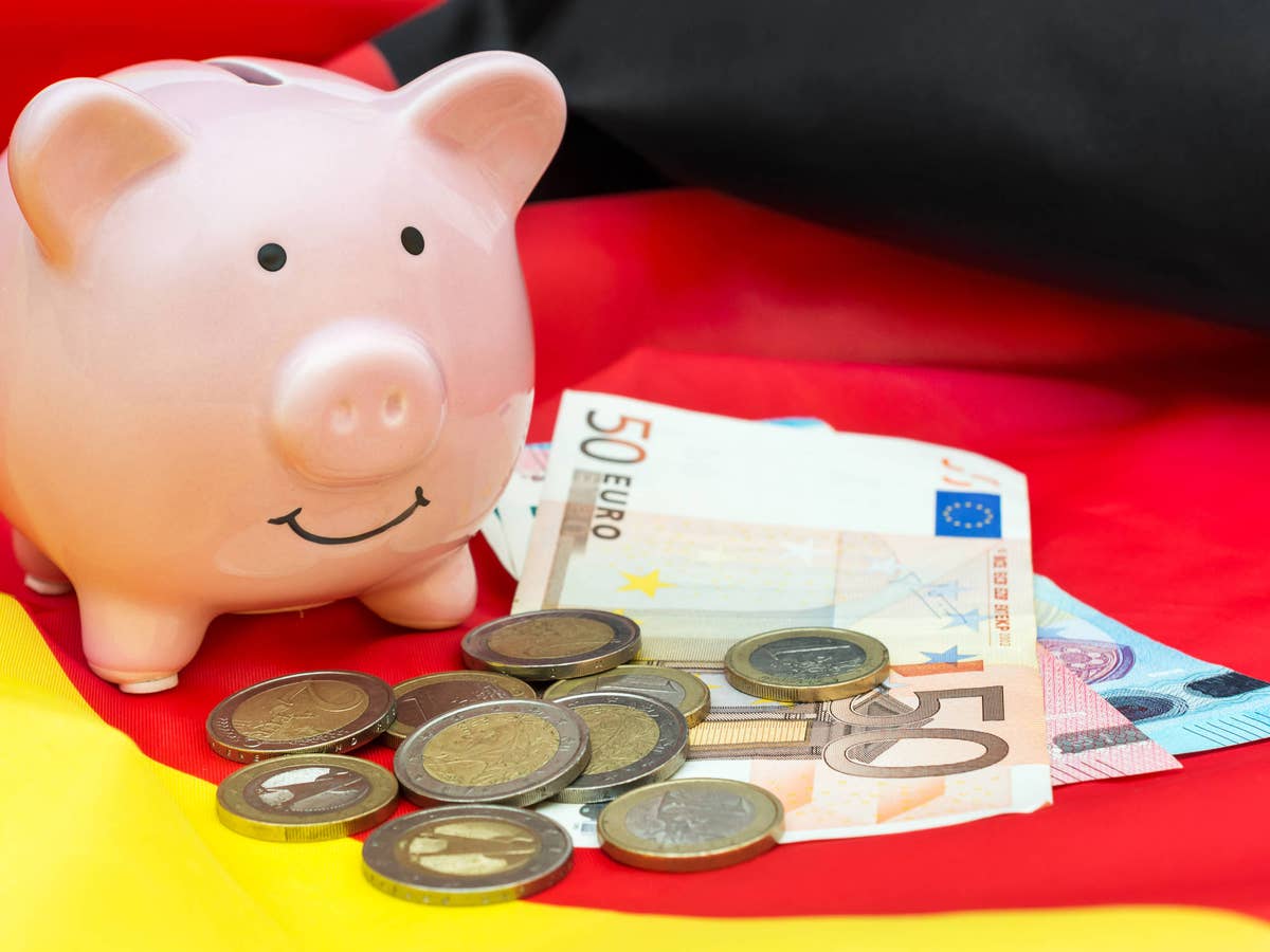 Sparschwein steht mit Euromünzen und Geldscheinen auf einer Deutschland-Flagge.