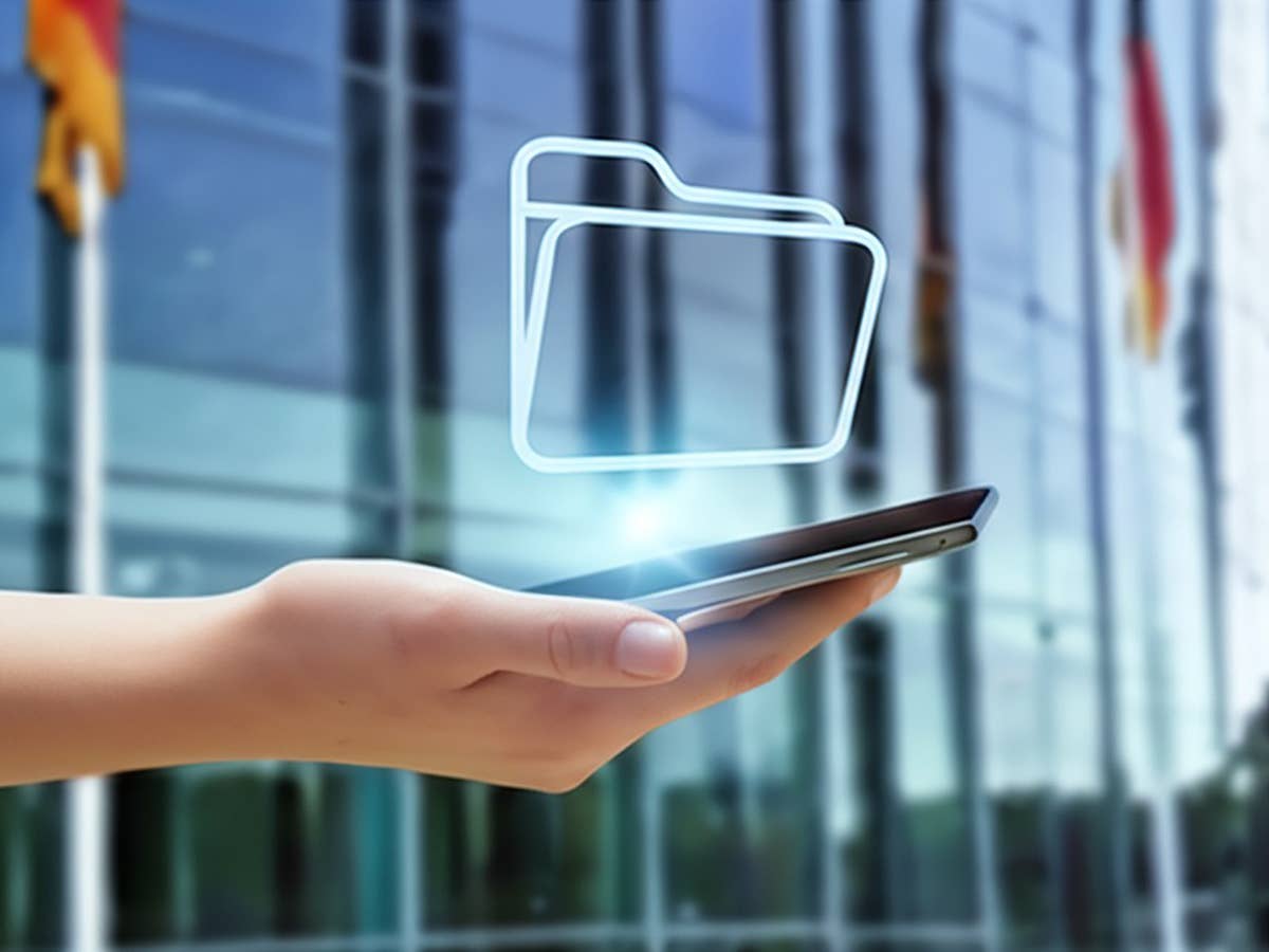 Eine Hand hält ein Smartphone mit einem schwebenden Ordnersymbol vor einem modernen Gebäude.