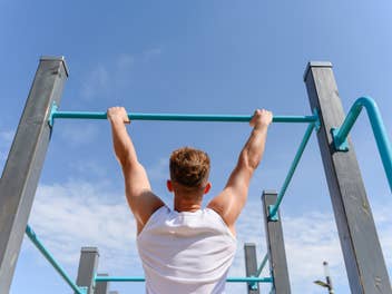 Eine Person, die unter einem blauen Himmel Klimmzüge an einer Stange macht.