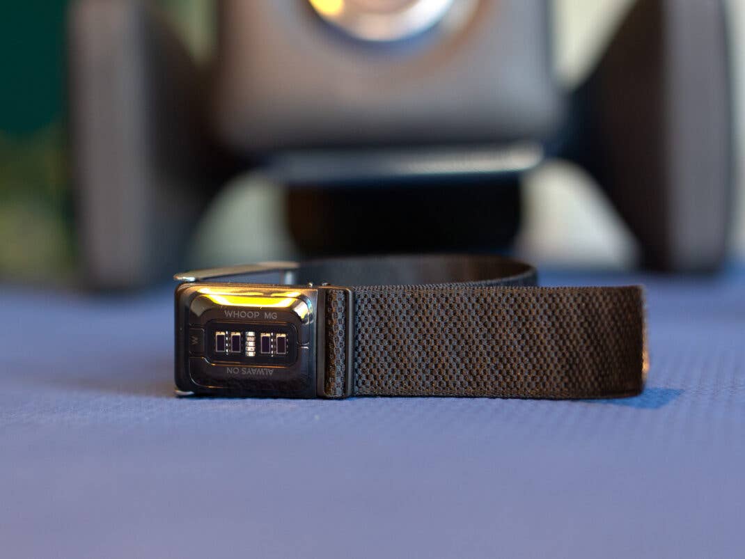 Nahaufnahme eines Whoop MG Sensors auf einem schwarzen Armband, das auf einer strukturierten Oberfläche liegt.