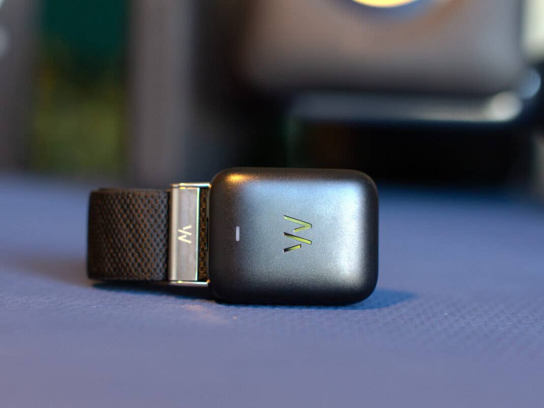Ein Whoop MG-Sensorgerät liegt auf einer blauen Oberfläche mit einem schwarzen Armband.