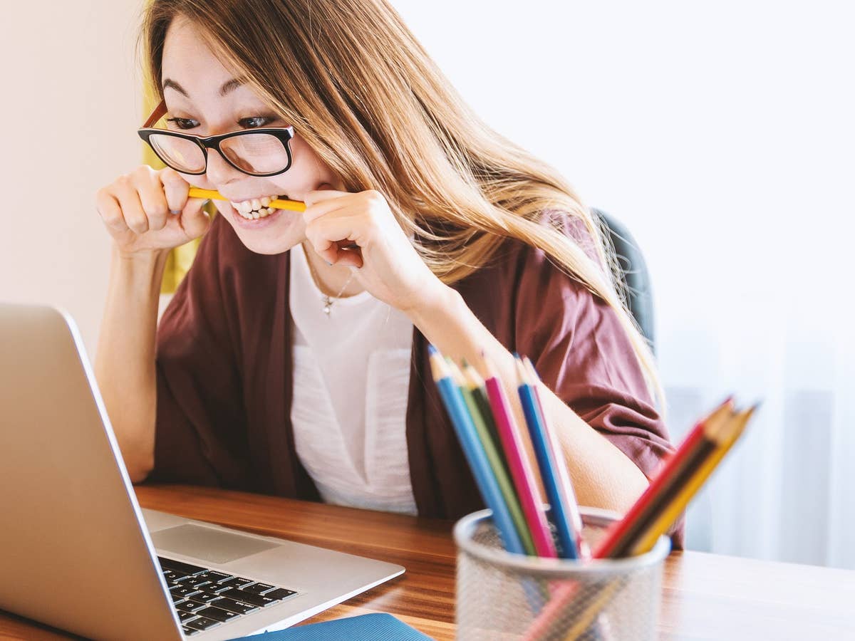 Eine Frau sitzt vor einem Laptop und beißt auf einen Stift