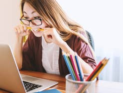 Eine Frau sitzt vor einem Laptop und beißt auf einen Stift